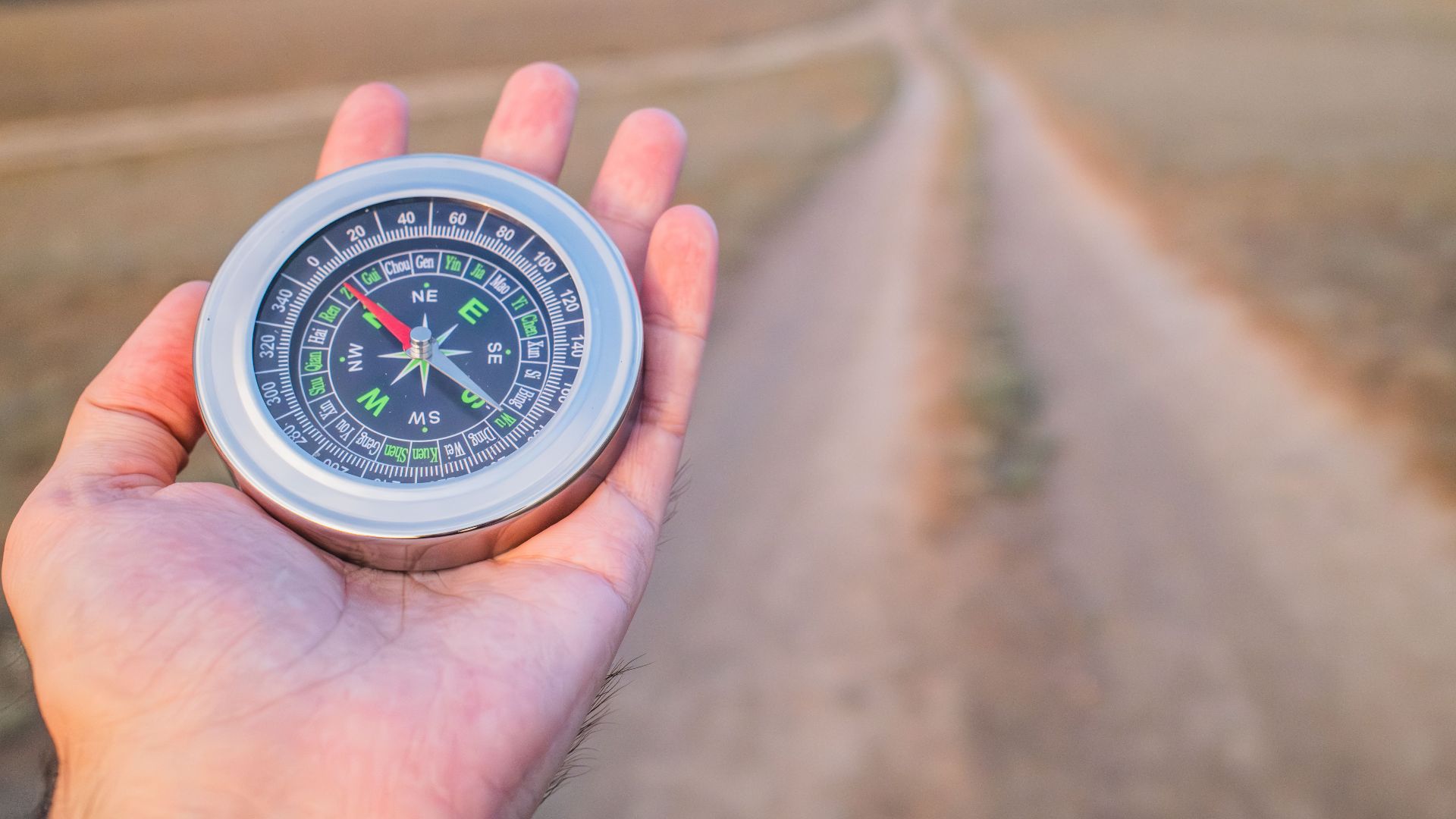 Hand holding a compass guiding along a dusty path outdoors. Perfect for travel and exploration themes.