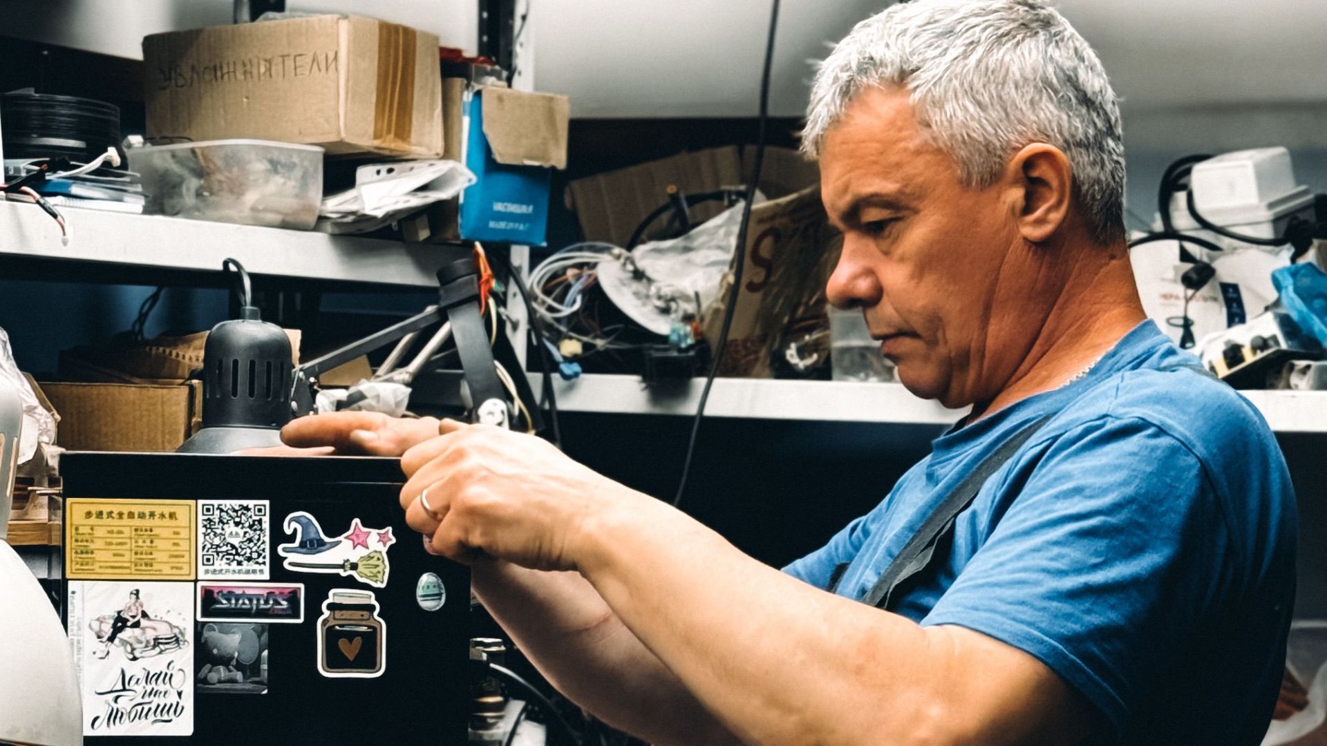 Senior man repairing equipment in a cluttered workshop filled with tools.
