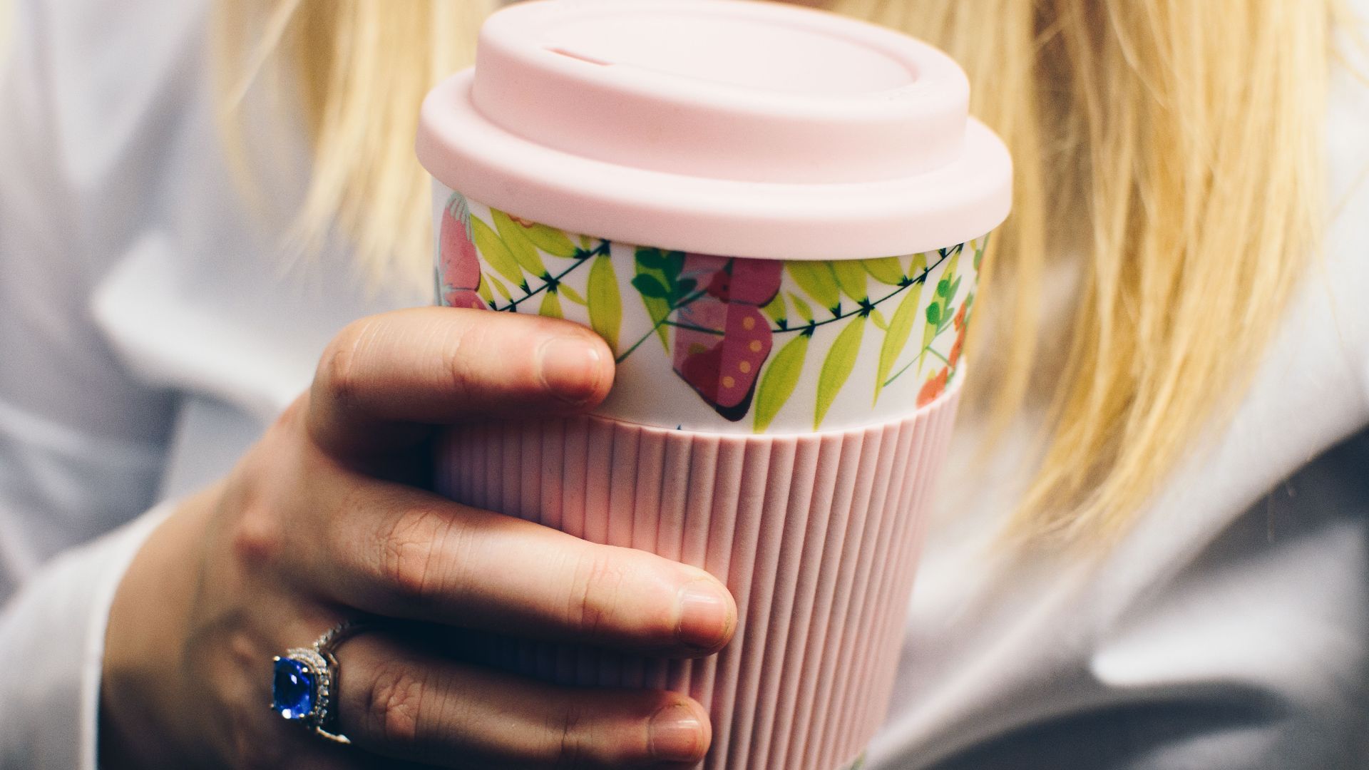 Close-up of a woman holding a reusable floral coffee cup, showcasing eco-friendly lifestyle.