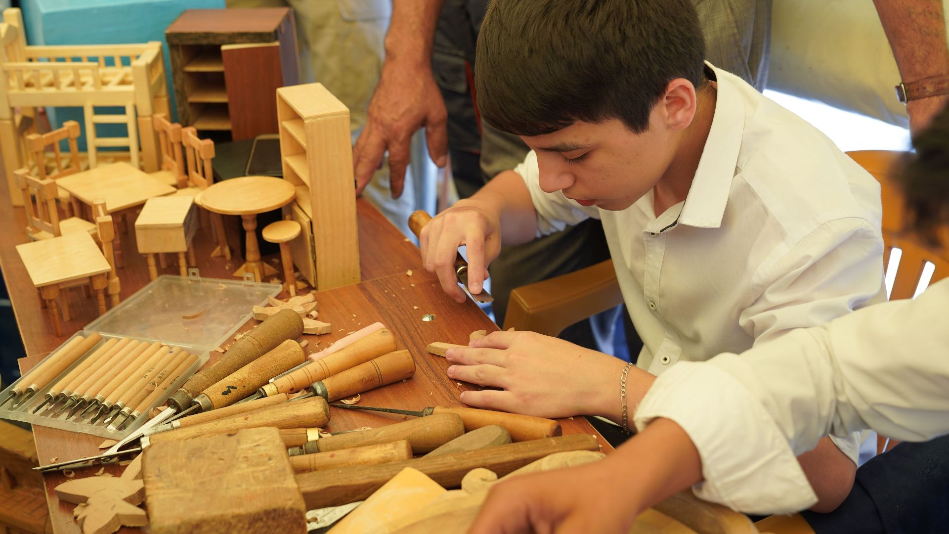 Teen boy focused on crafting detailed wooden models with carving tools, showcasing traditional woodworking skills.