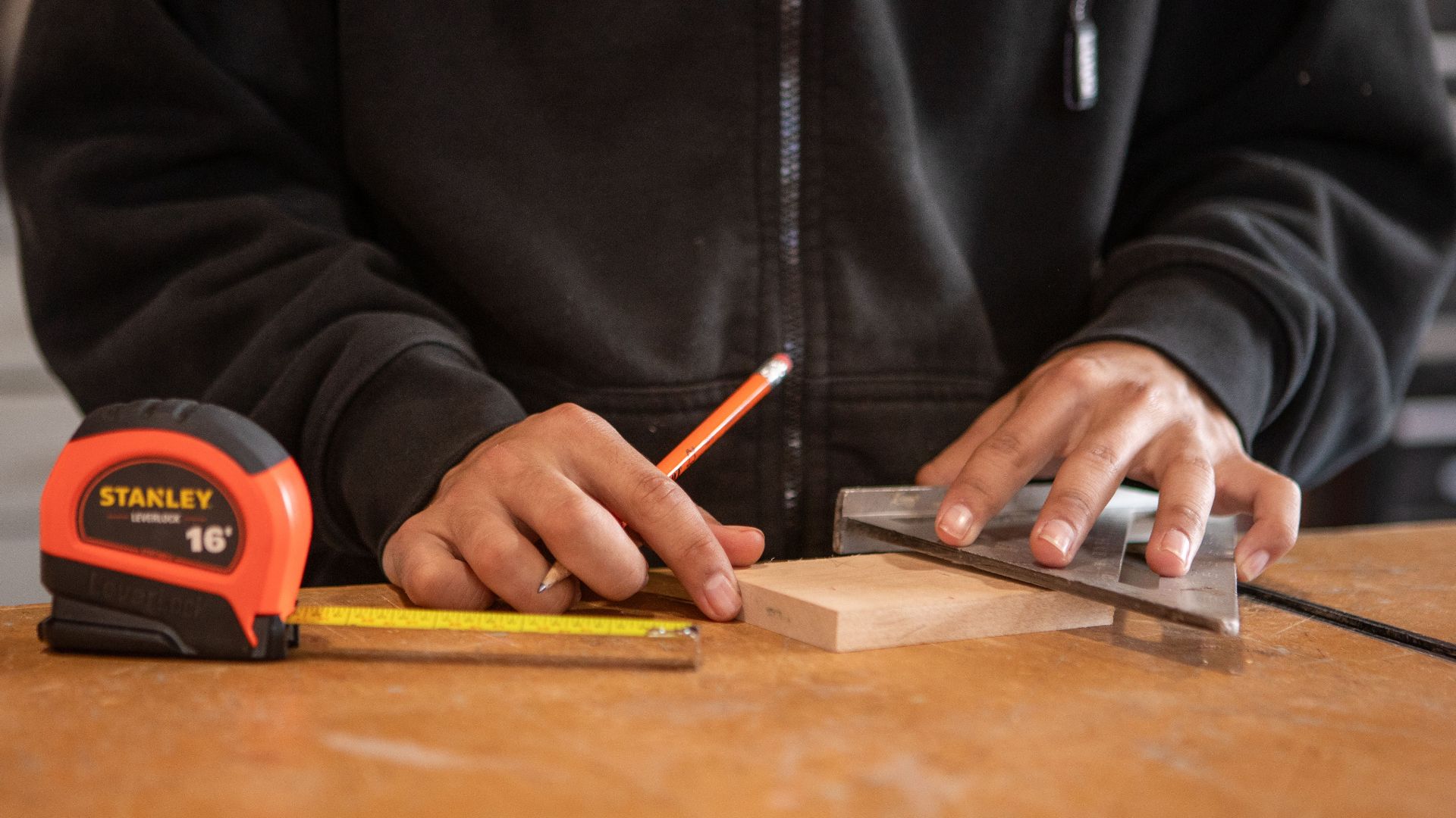 Carpenter using tape measure and speed square on wood block, ensuring accurate measurements.