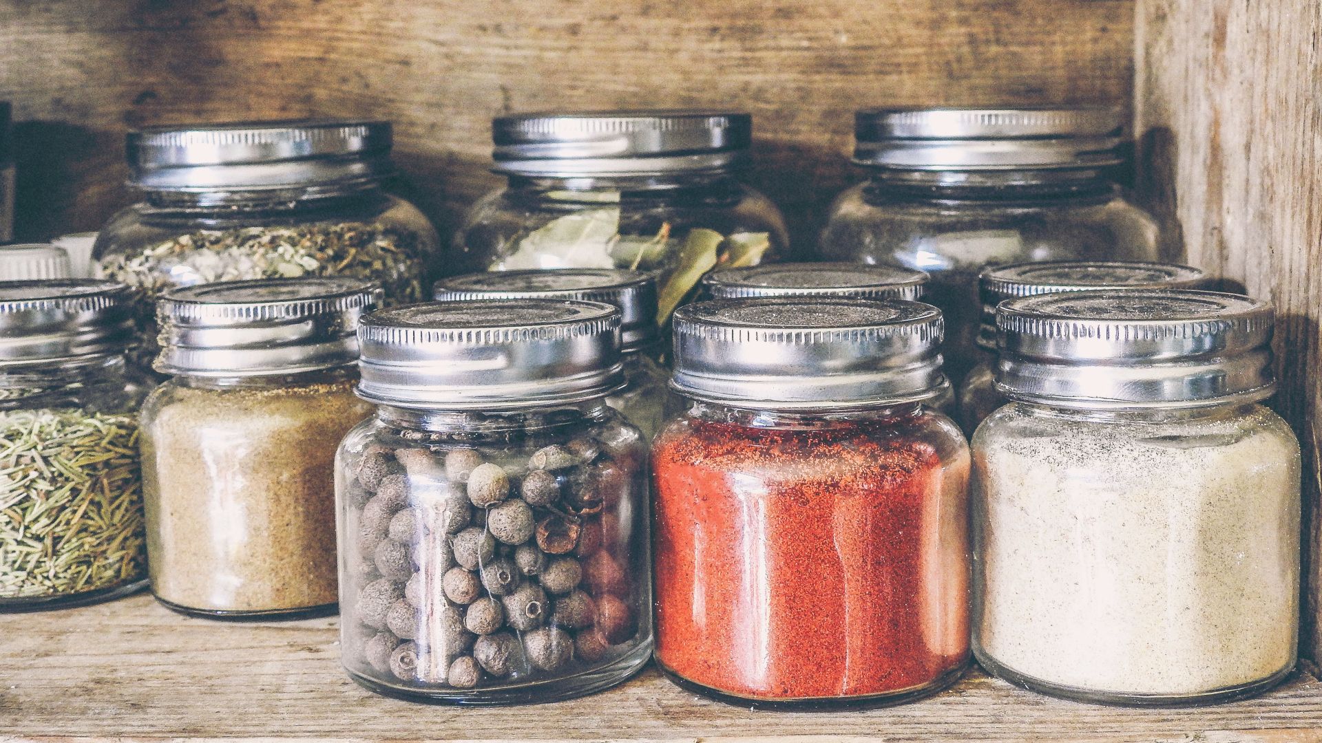A collection of assorted spices in glass jars on a rustic wooden shelf for culinary use.