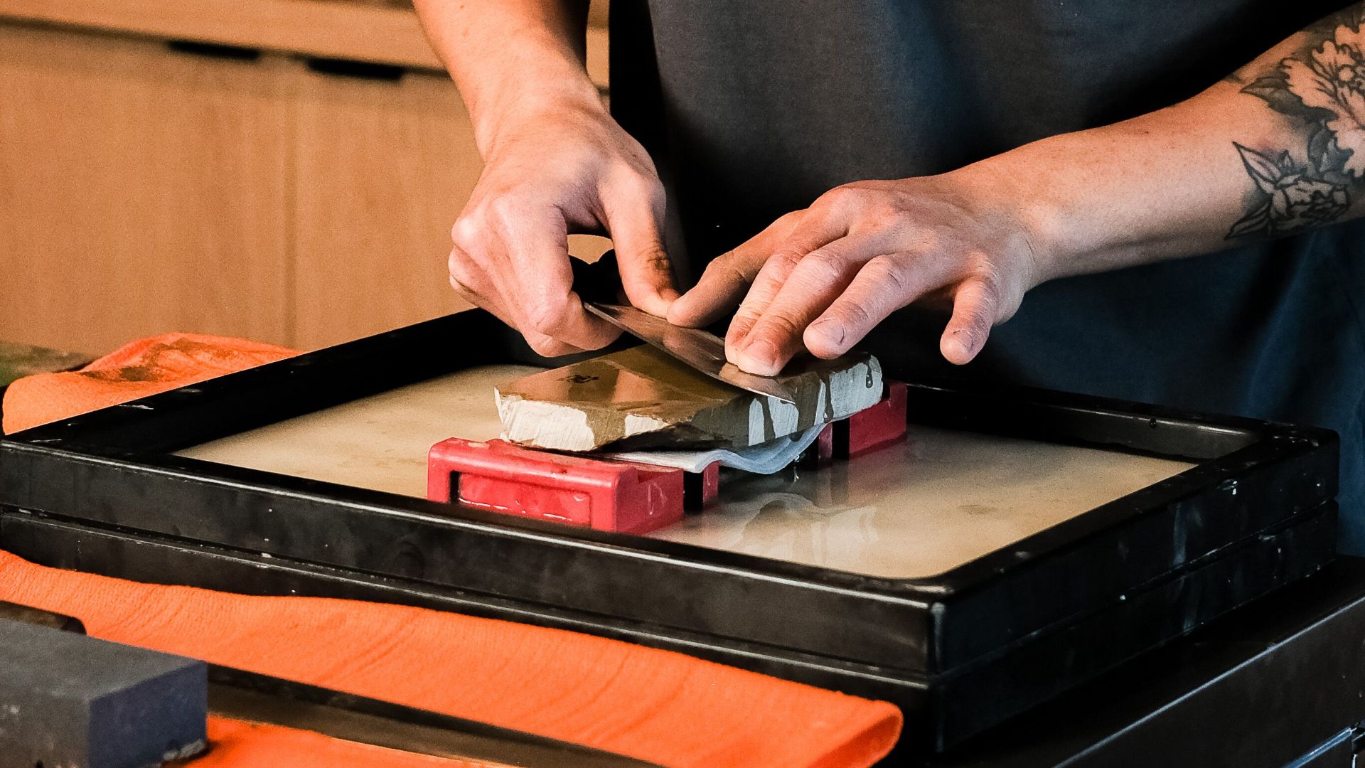 Asian chef sharpening a knife indoors using a whetstone in a Japanese restaurant setting.