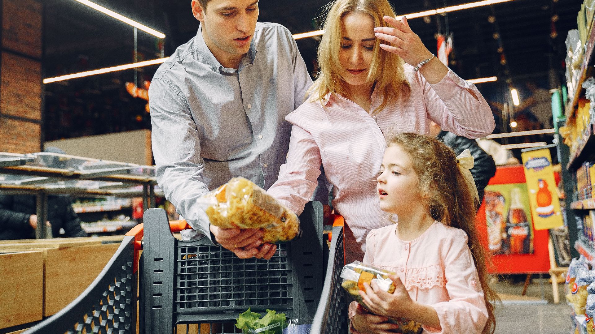 A family enjoying shopping in a supermarket aisle, selecting groceries with a cart.