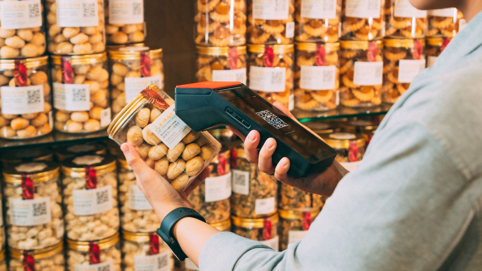 Individual scanning QR codes on jars in a store with a handheld device.