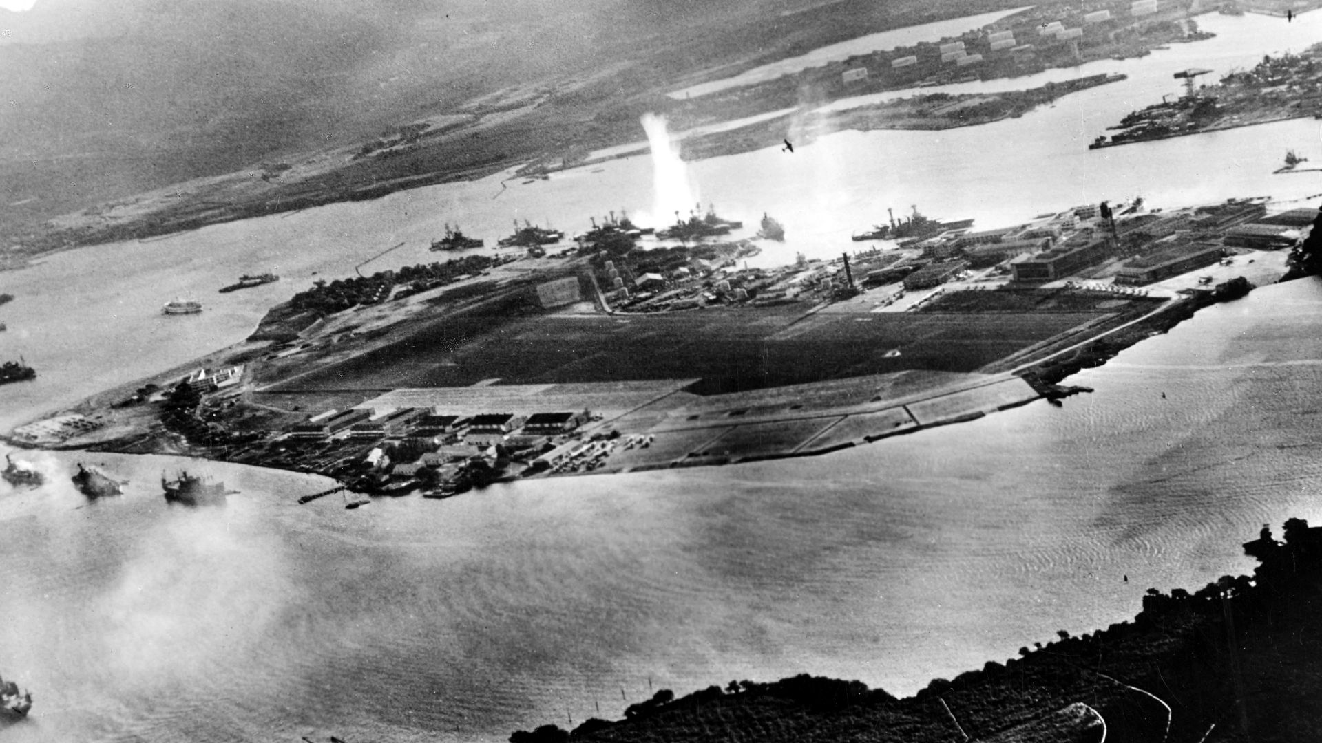Photograph taken from a Japanese plane during the torpedo attack on ships moored on both sides of Ford Island shortly after the beginning of the Pearl Harbor attack. View looks about east, with the supply depot, submarine base and fuel tank farm in the ri