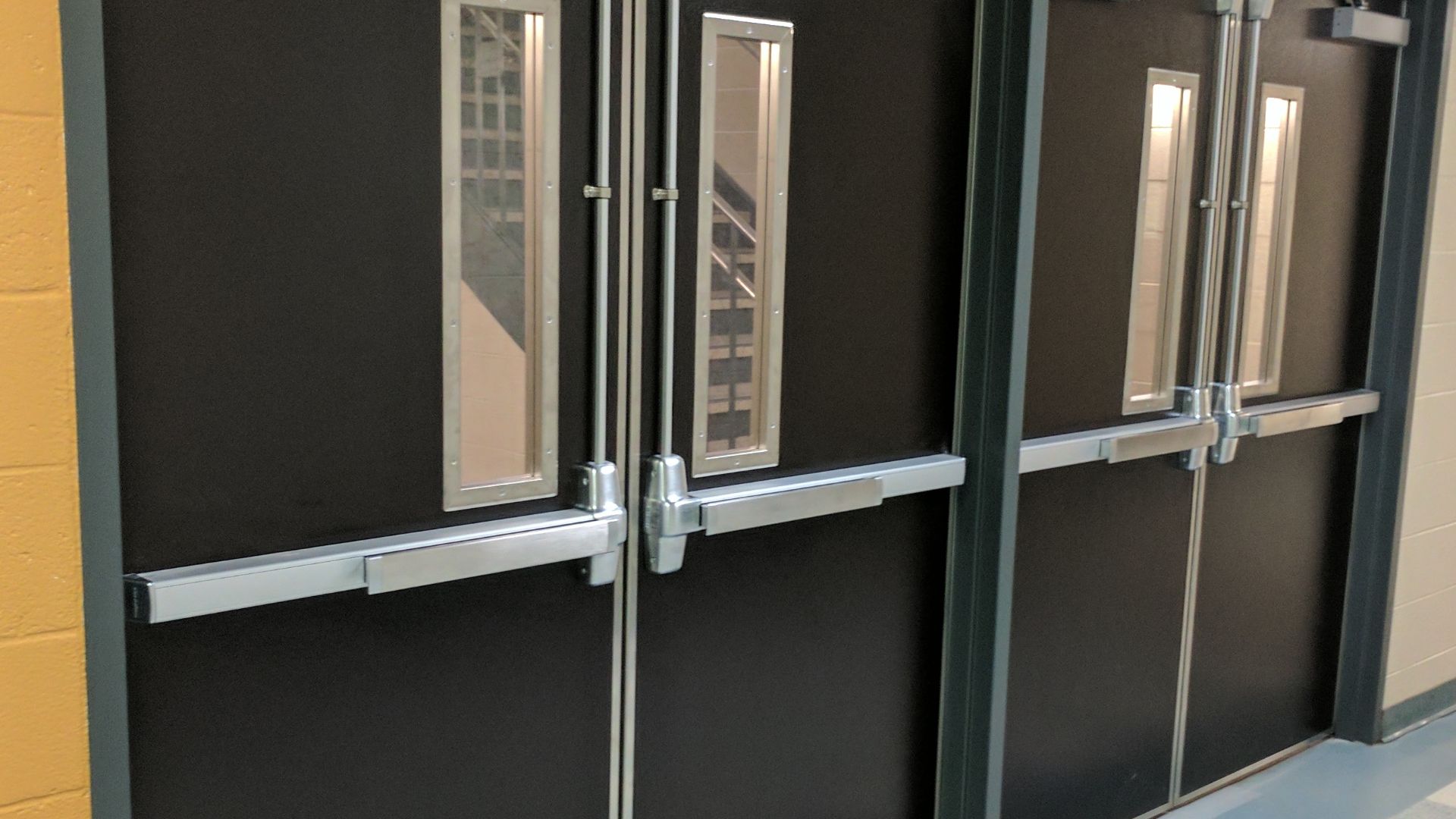 A set of doors in a US school fitted with push bars (aka. panic or crash bars) and upper Pullman latches.
