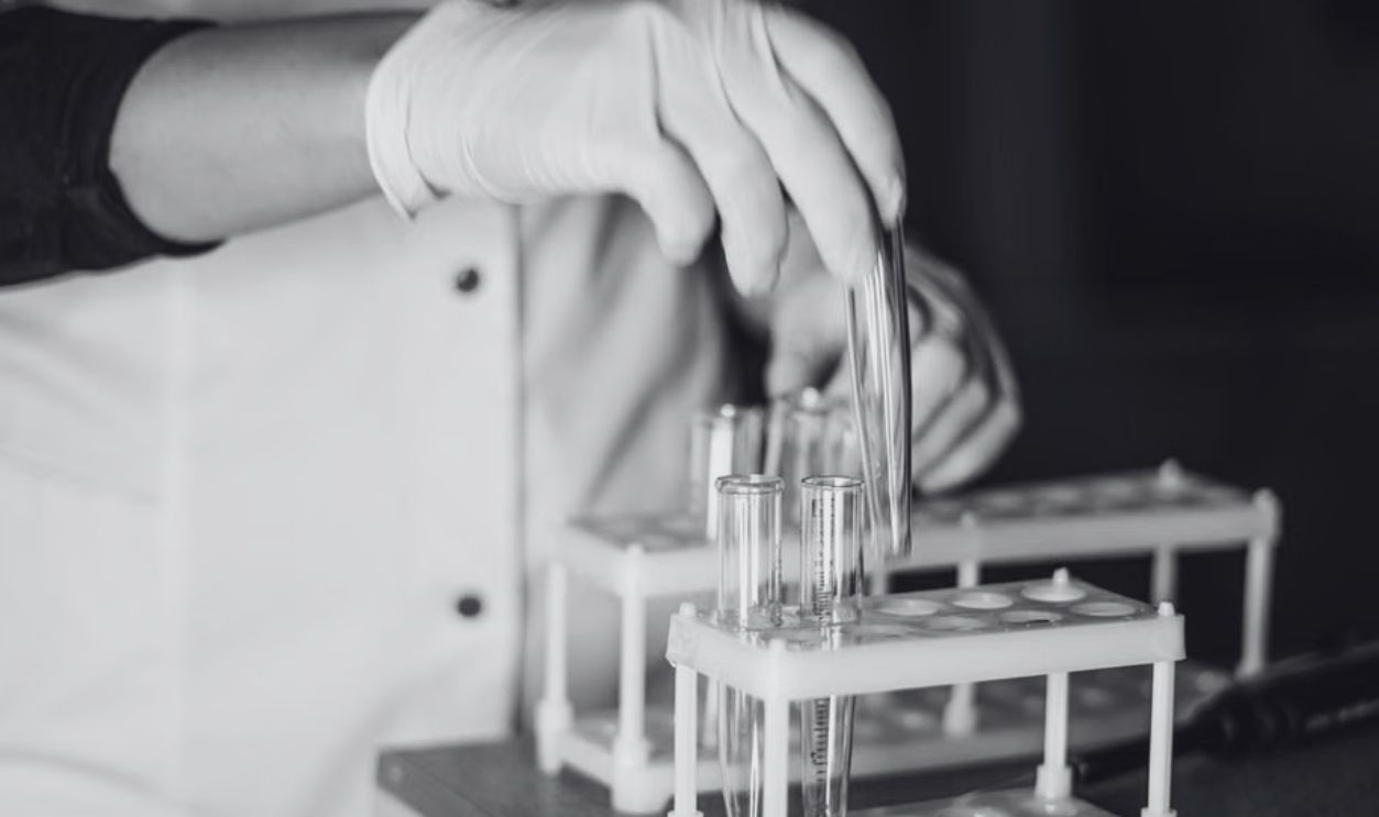 A scientist in a lab coat handling test tubes in a laboratory setting with a focus on equipment