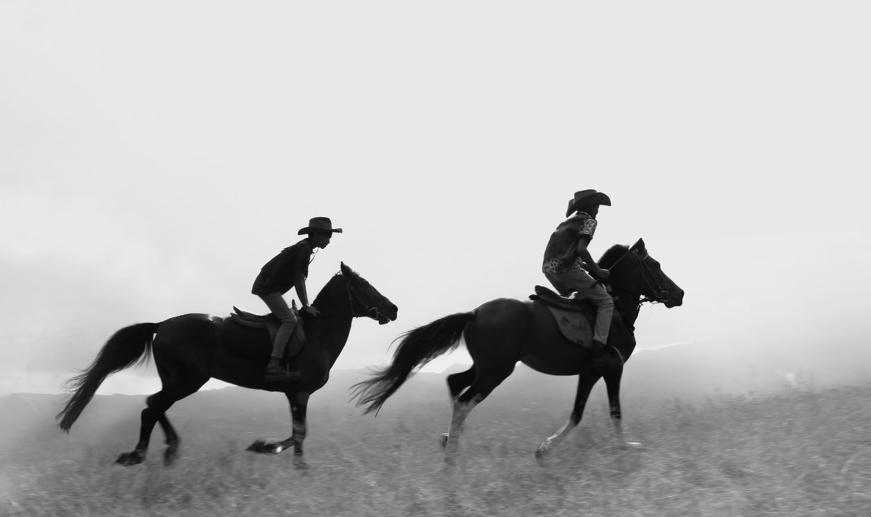 Two riders on horseback galloping across a misty plains, captured in dynamic black and white