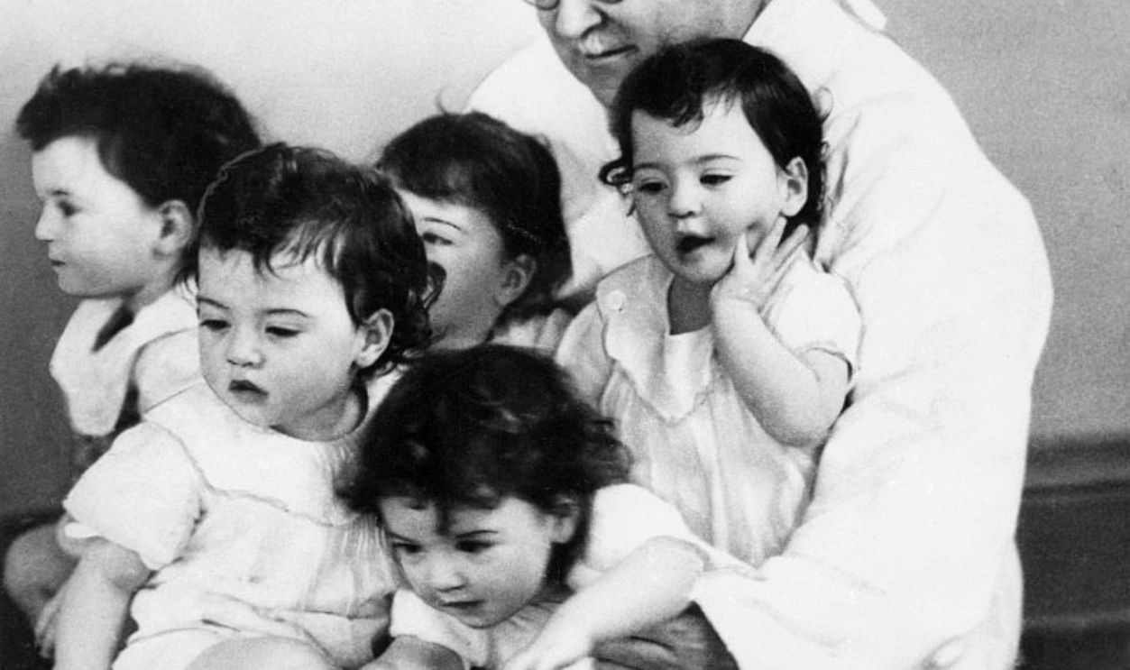 (Original Caption) 5/28/1935-Callender, Ontario: Honored guest Dr. Allan R. Dafoe puts his arms around all five of the Dionne quintuplets -- Marie, Emelie, Cecile, Annette and Yvonne -- as they celebrate their first birthday in style.