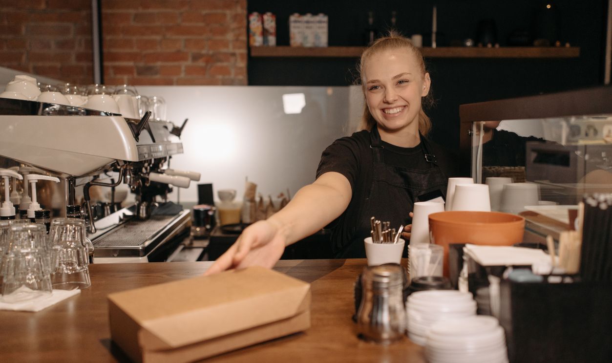 Smiling barista handing a takeout box at a modern coffee shop counter