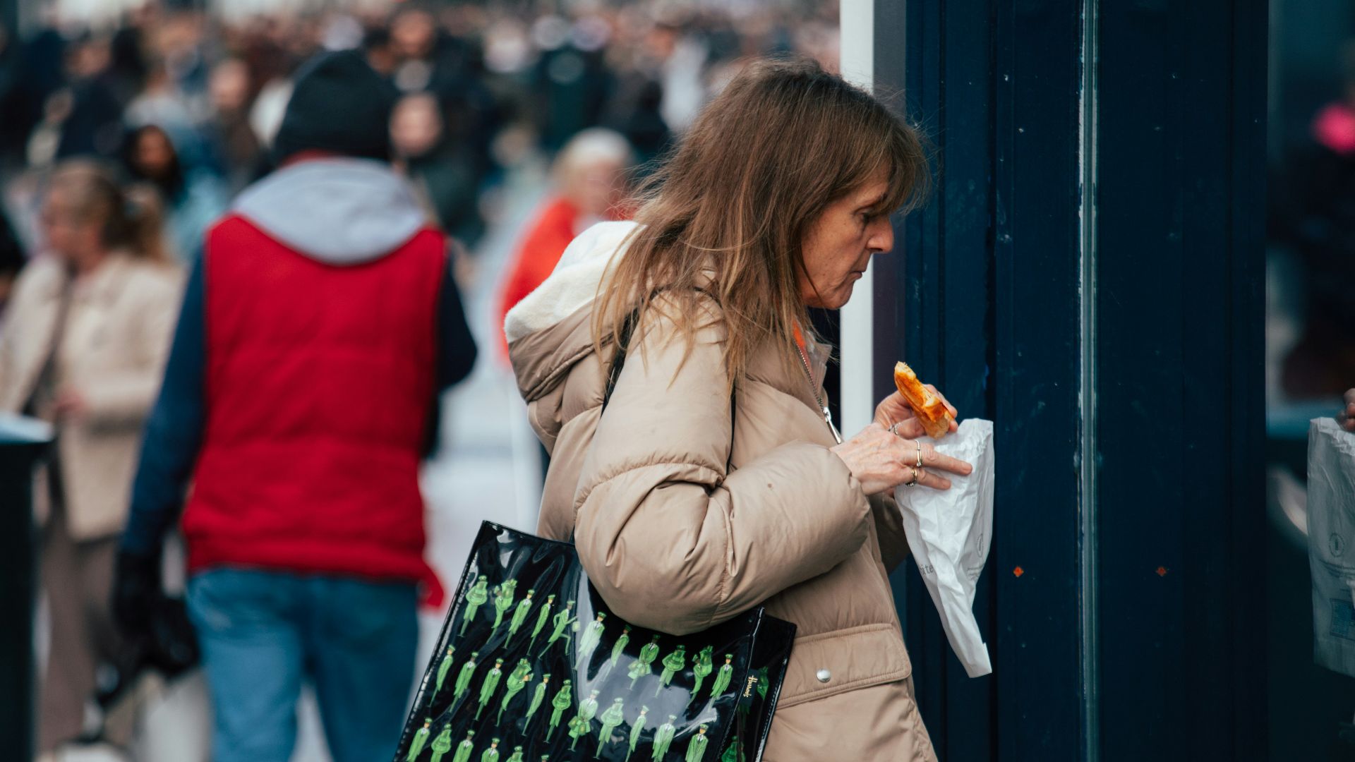 Woman in puffer jacket eating outdoors with shopping bag