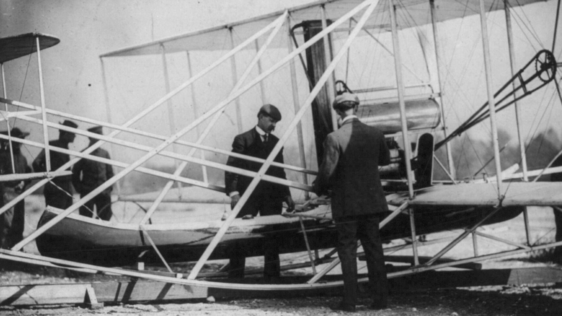 Title: Wilbur Wright examining canoe attachment to aeroplane before 1st flight over water
Abstract/medium: 1 photographic print.