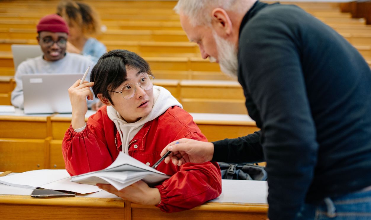 A professor assisting a college student during class in a university lecture hall