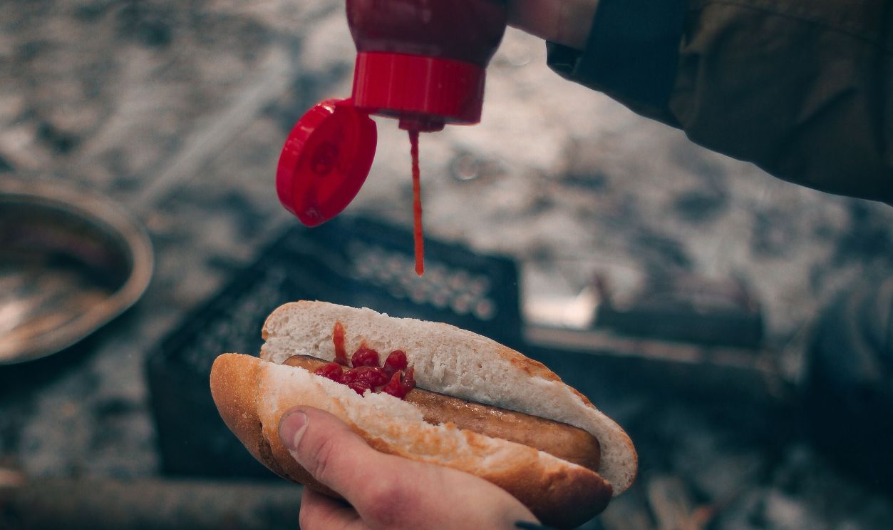 A cozy winter scene of a hotdog being topped with ketchup over a campfire, capturing outdoor culinary adventure
