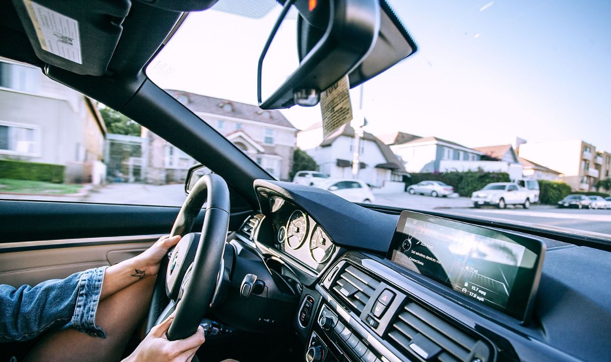 Woman in denim jacket driving through a sunny suburban neighborhood, highlighting modern lifestyle