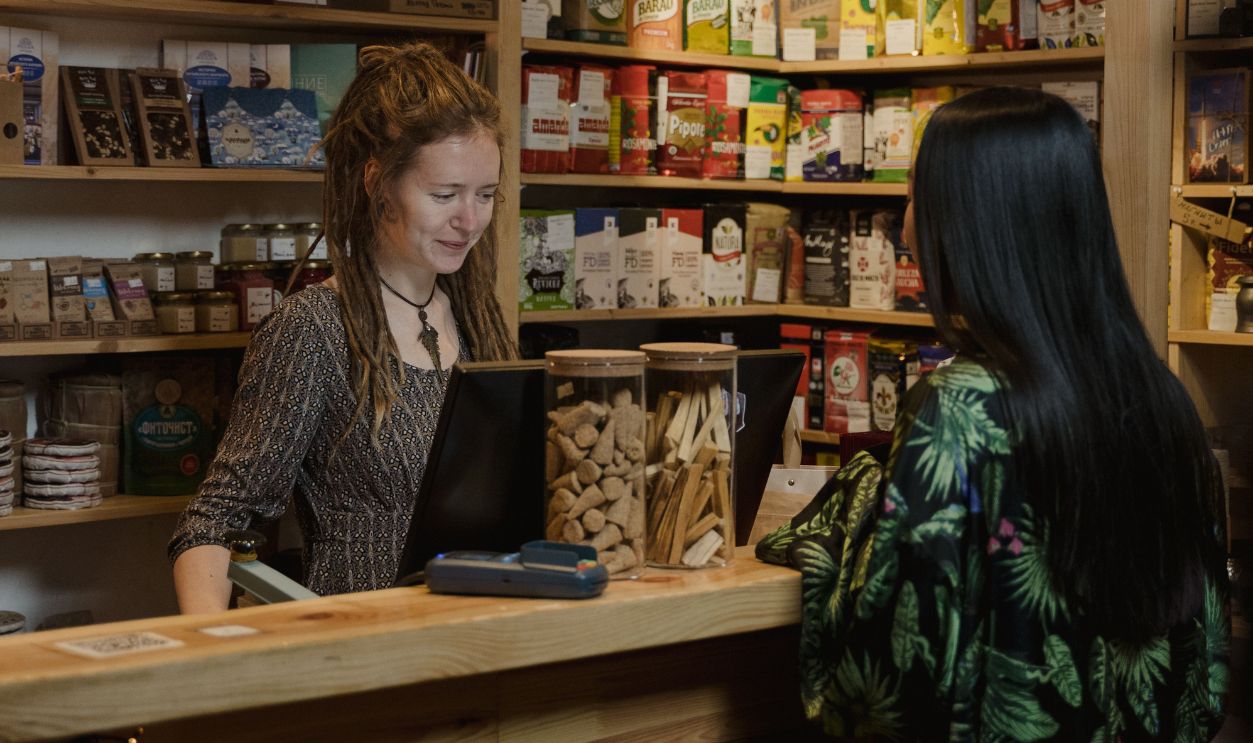Woman customer interacting at a wood-accented store checkout, surrounded by various merchandise.