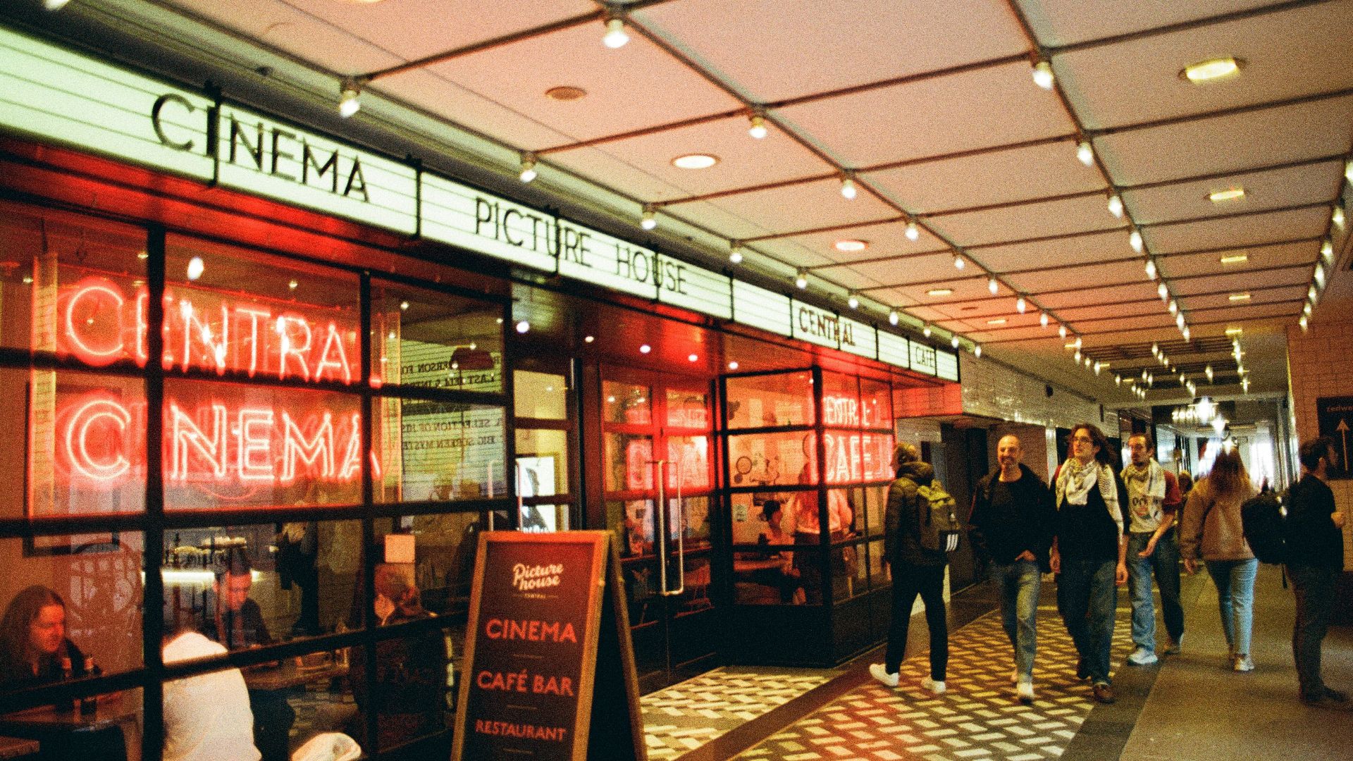 People walking past a cinema with bright red neon signs