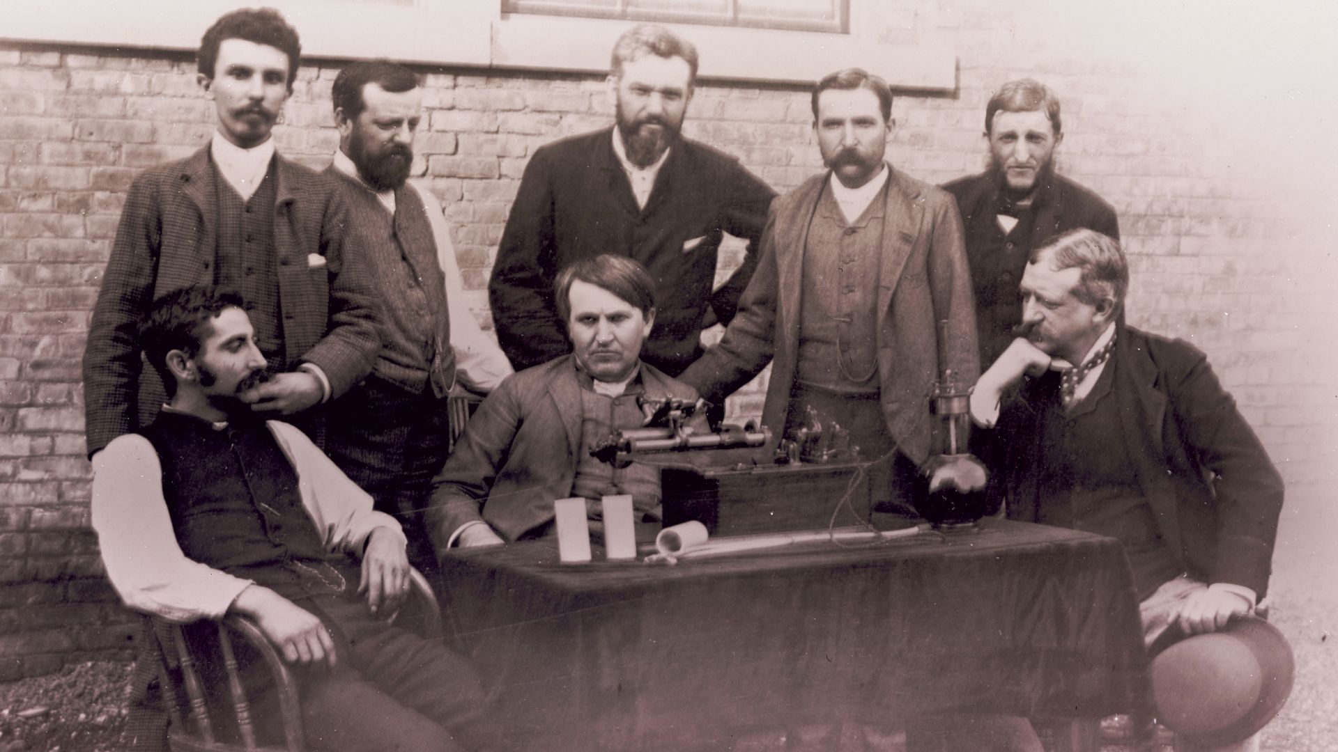 Thomas Edison posing with the group who perfected the phonograph, with the phonograph on the table. Edison is seated in the center, Theo Wangemann is standing behind him.