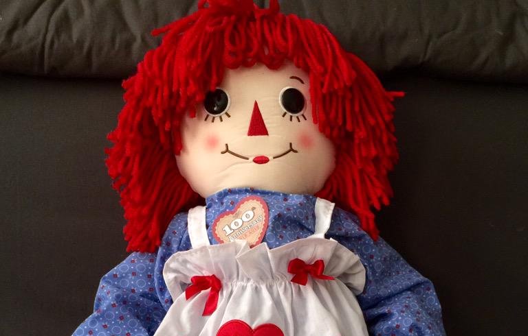 Photo of Raggedy Ann a rag doll with red yarn for hair and has a triangle nose