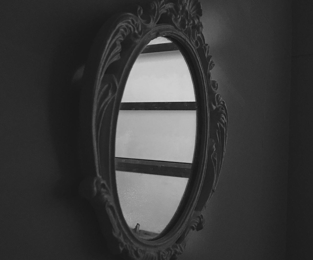 Grayscale Photo of Oval Mirror hanging on a wall