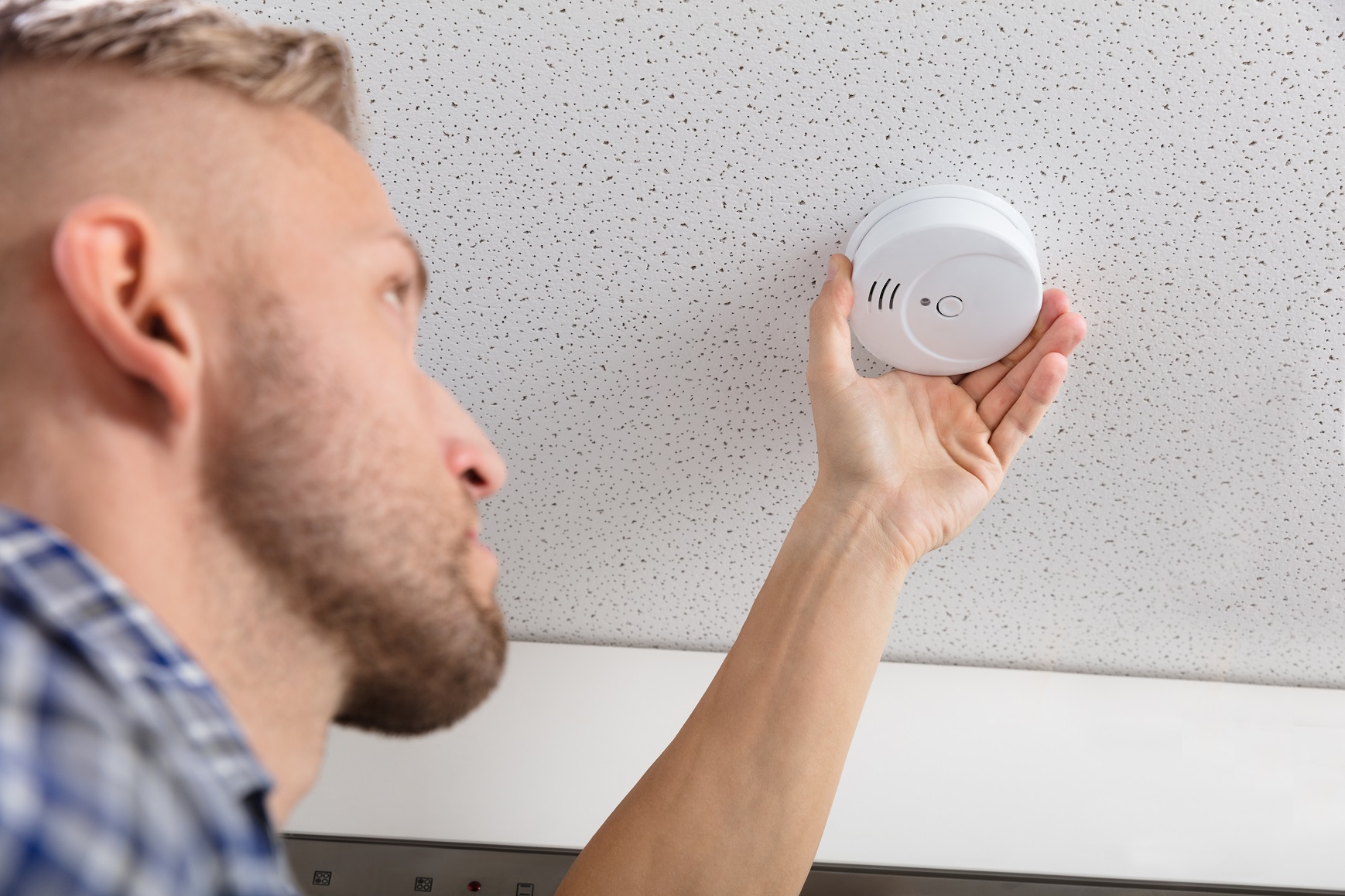 Person's Hand Installing Smoke Detector On Ceiling