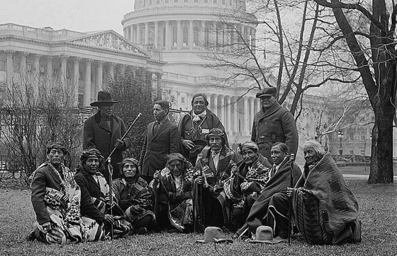 A group of Osage people sitting in front of a building - 1923