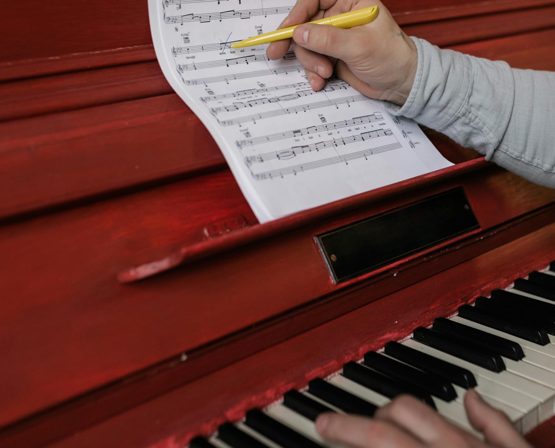 Person Writing on the Sheet Music Placed on Piano