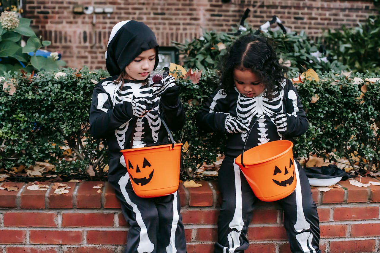 Little multiracial girls in skeleton costumes sitting with candy bucket