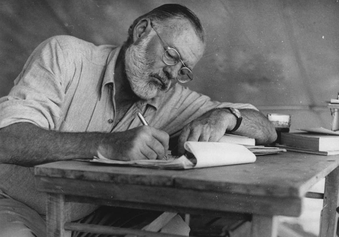 Ernest Hemingway sitting at a table writing - 1934