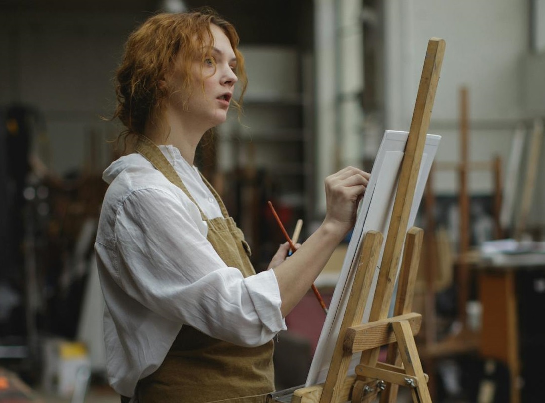 Young Woman in Brown Apron Sketching on White Cardboard