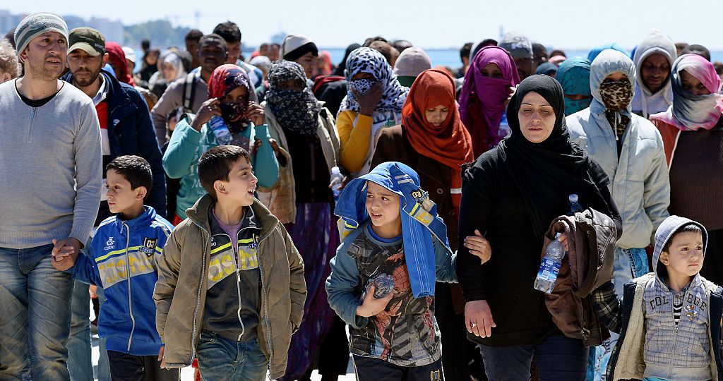 Rescued migrants walk along the quayside after disembarking from the Italian Navy vessel Bettica