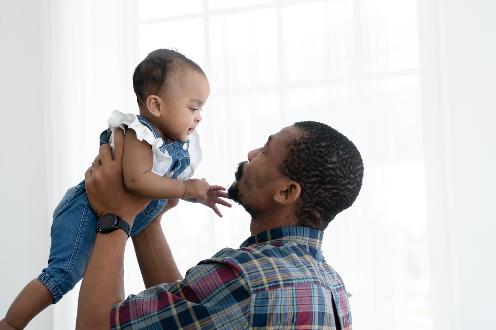 African father with beard tossing  his newborn baby girl up in the air and playing together