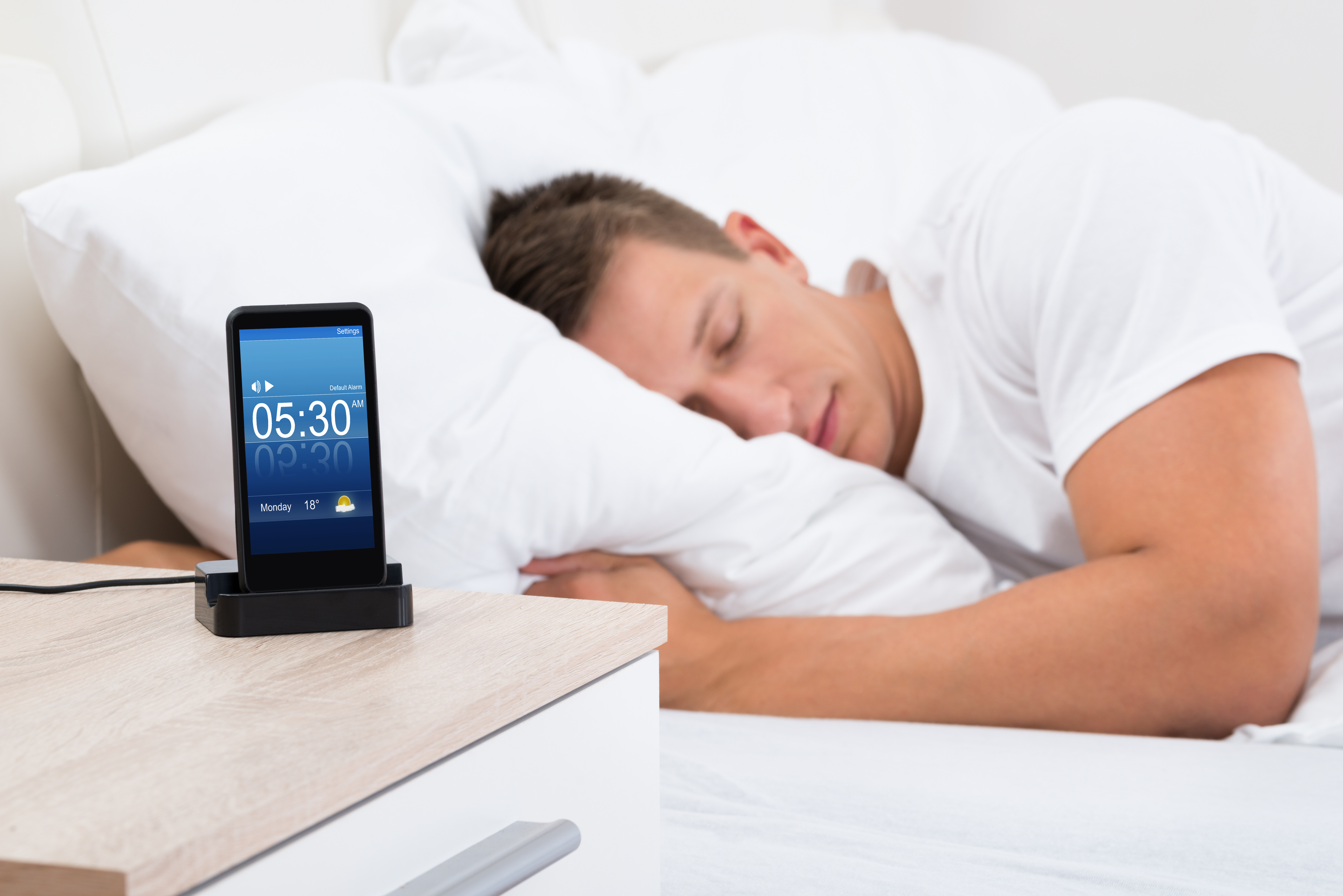 Man sleeping beside alarm clock on iphone