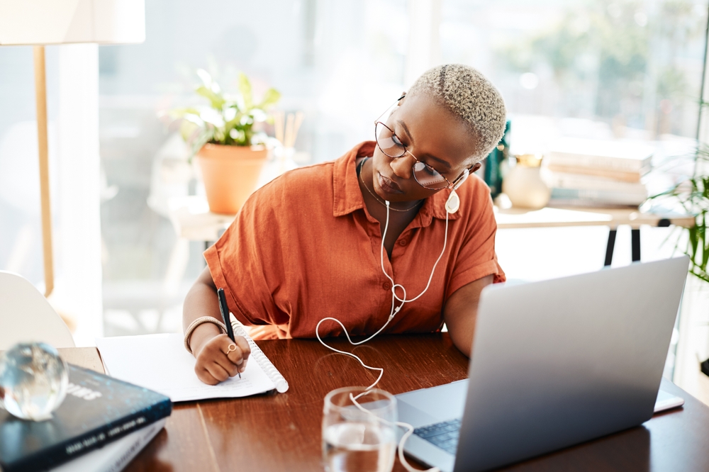 Young businesswoman wearing earphones while writing notes in an office.