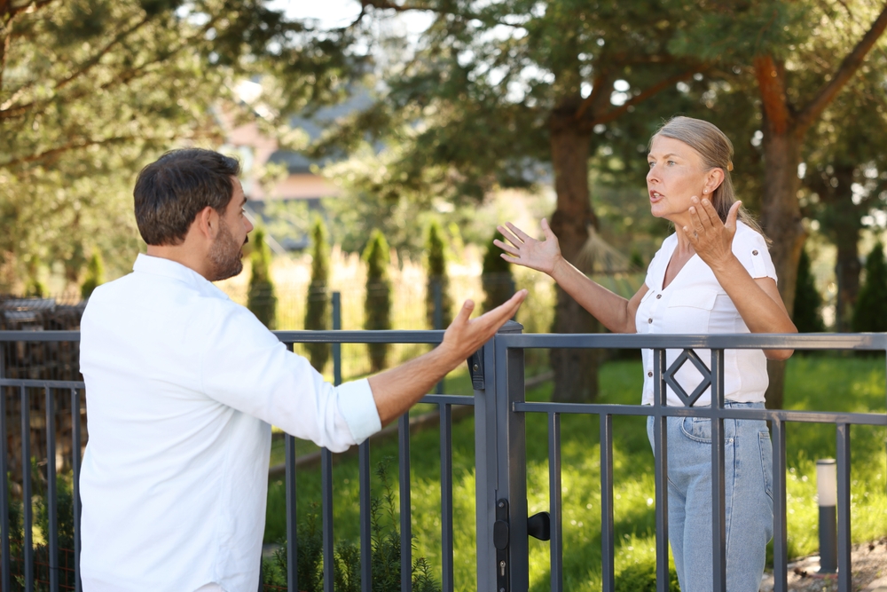 Emotional neighbours having argument near fence outdoors