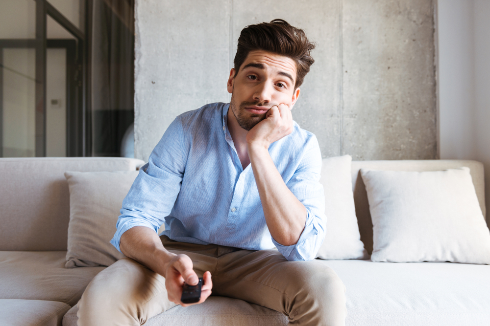 Portrait Photo of Bored young man holding tv remote control