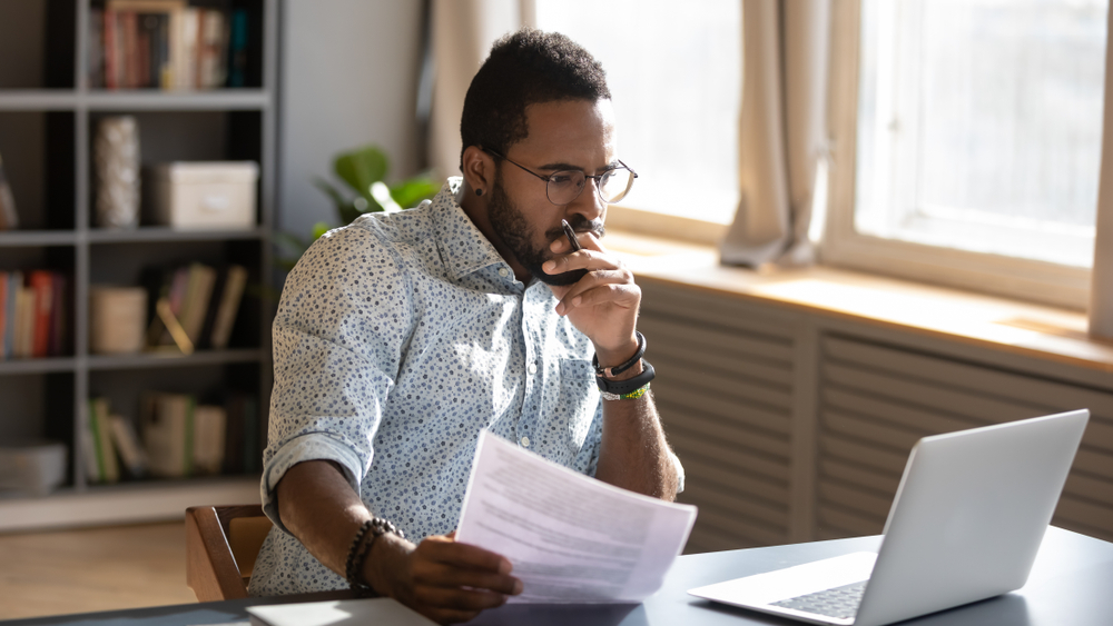 Focused serious businessman holding documents an looking at laptop