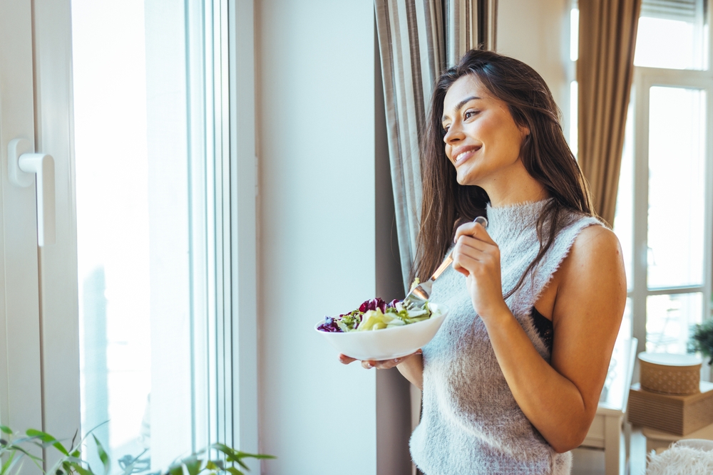 Portrait of a young and cheerful woman eating healthy salad