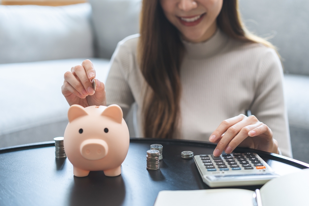 Young business woman hand putting coin into piggy for saving cost