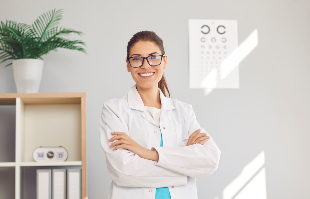 Portrait of happy young Caucasian female optician in white medical uniform pose in optics salon.