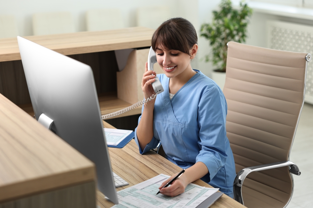 Smiling medical assistant talking by phone and working with documents in office