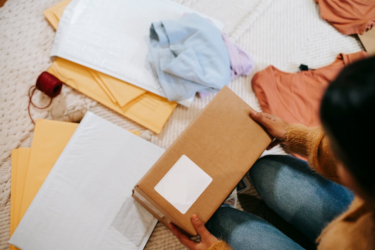 Woman unpacking parcel with address among envelopes and clothes