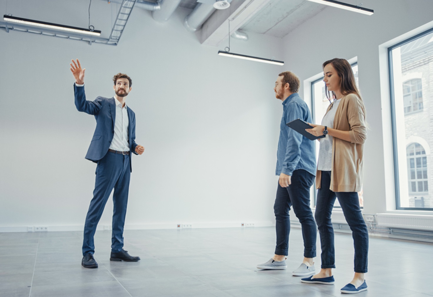 Real Estate Agent Showing a New Empty Office Space to Young Male and Female Hipsters.