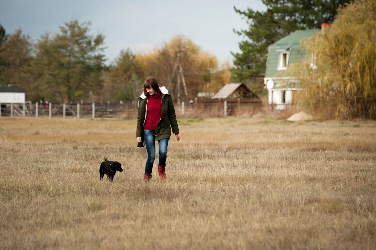Photo of Woman Walking Beside Short-coated Black Dog at Daytime