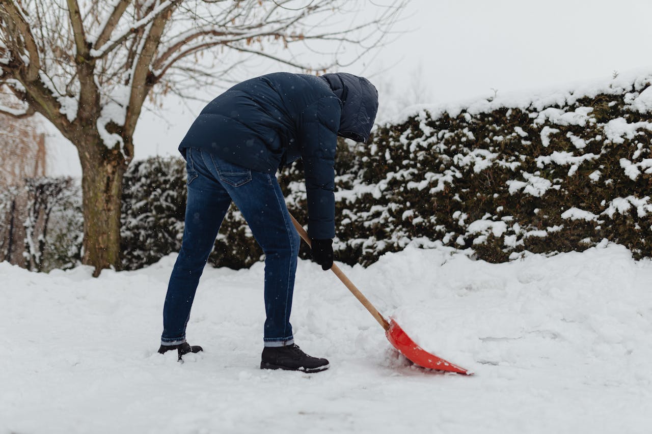 Photo of a Man in Blue outfit Shoveling Snow