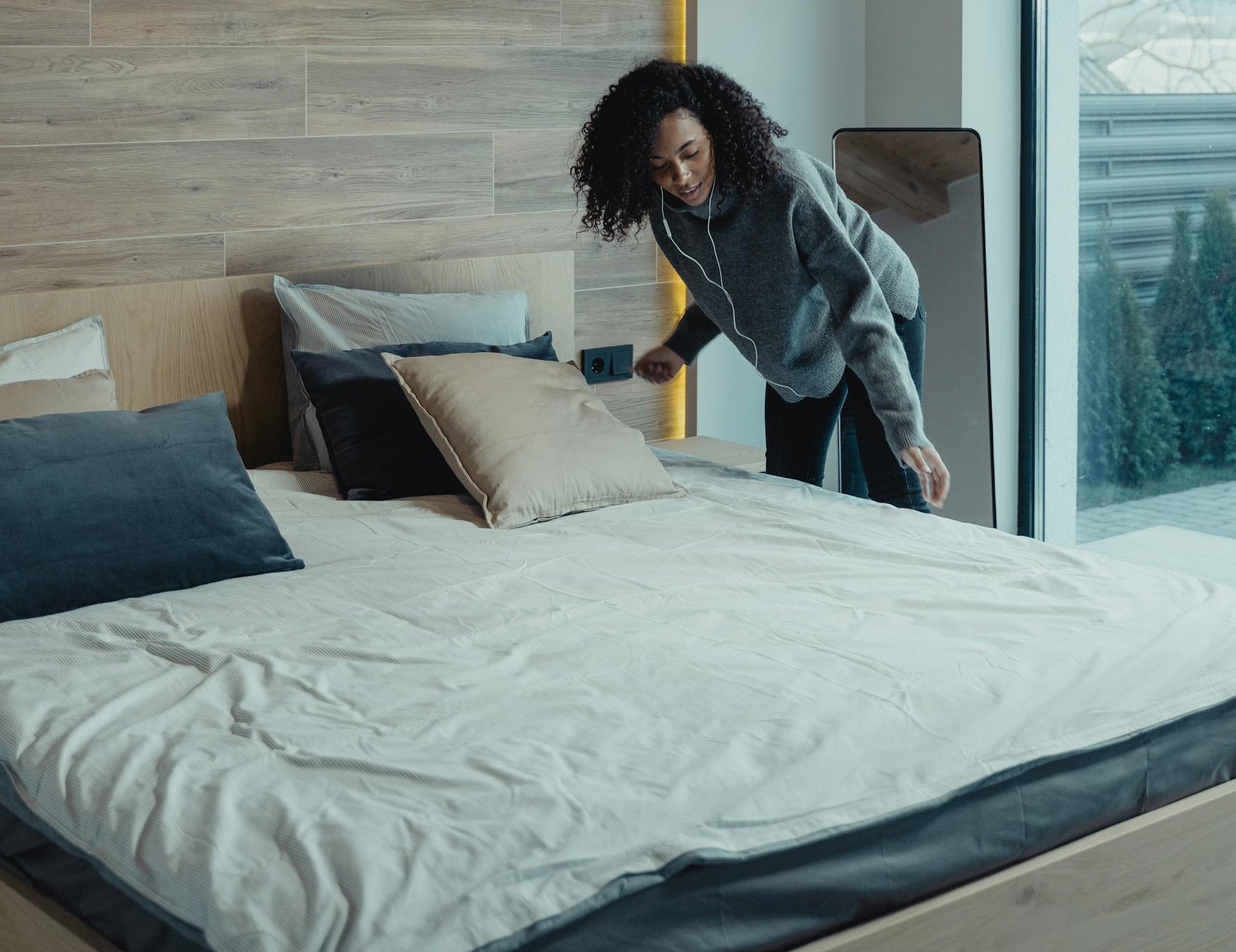 Portrait Photo of Woman in Gray outfit fixing her Bed