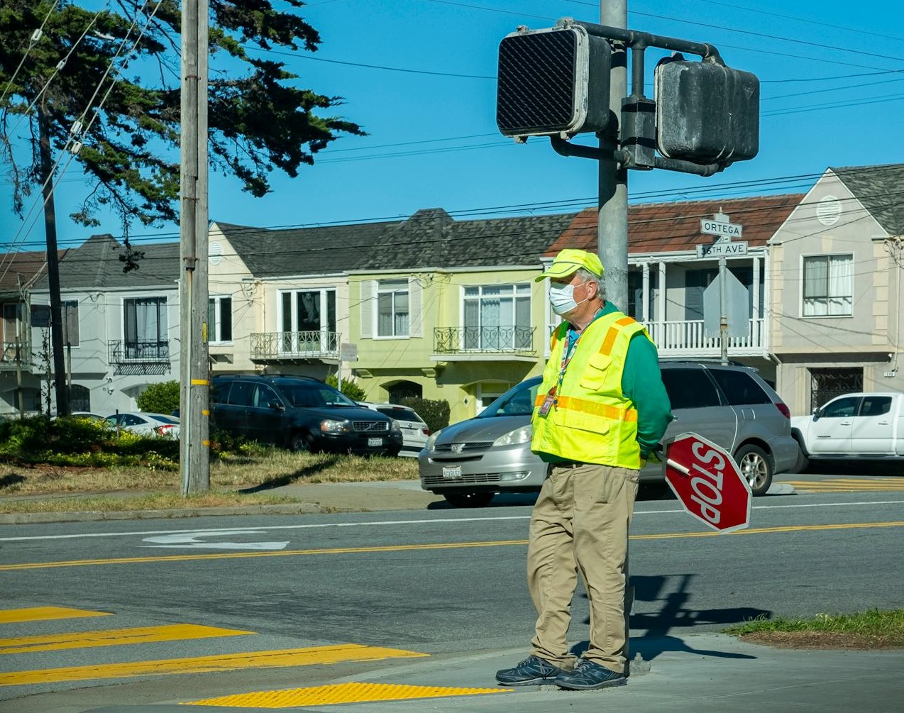Man in a Safety Vest Holding a Stop Sign Standing by a Traffic Light