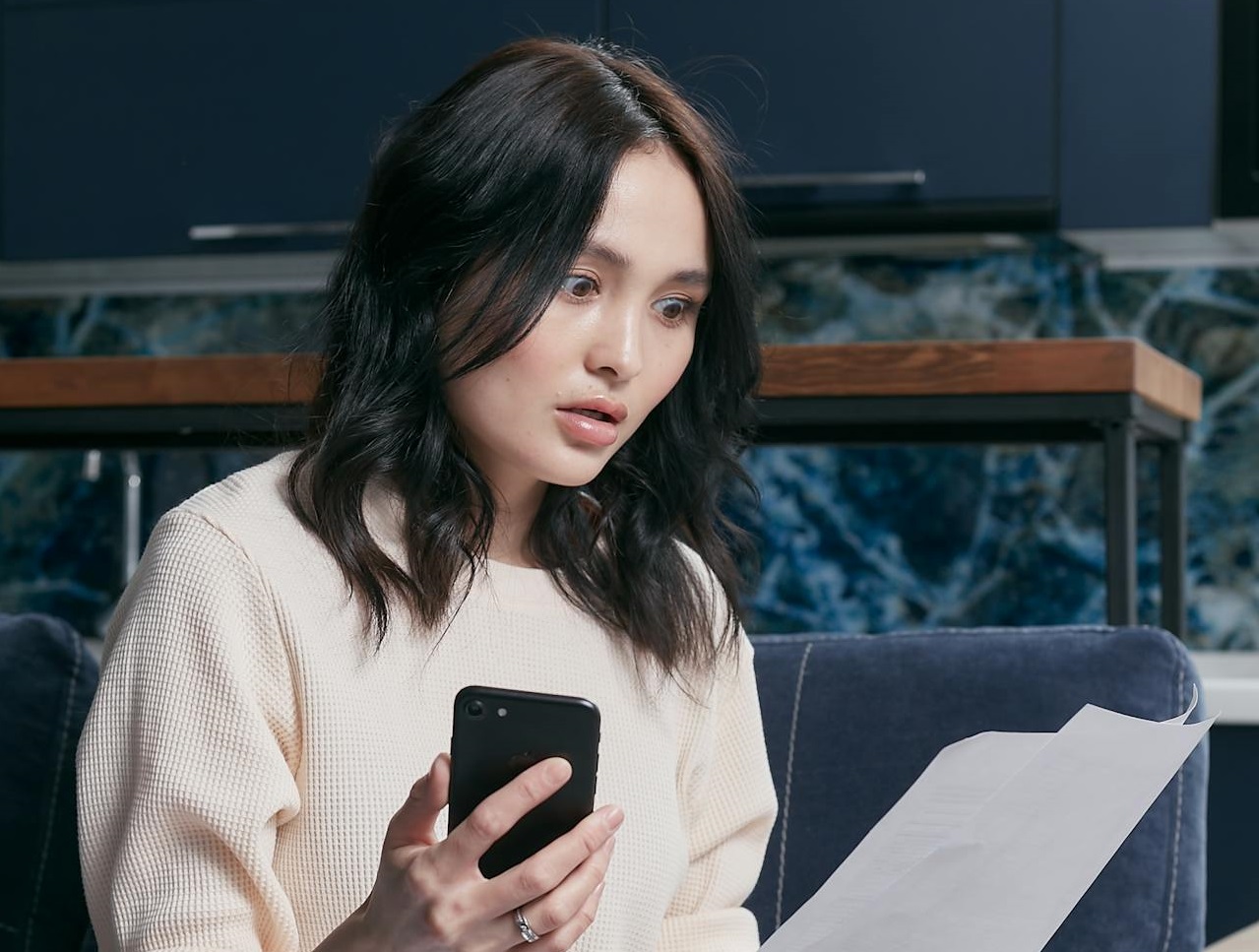 Surprised woman with paper and cell phone in the hands.