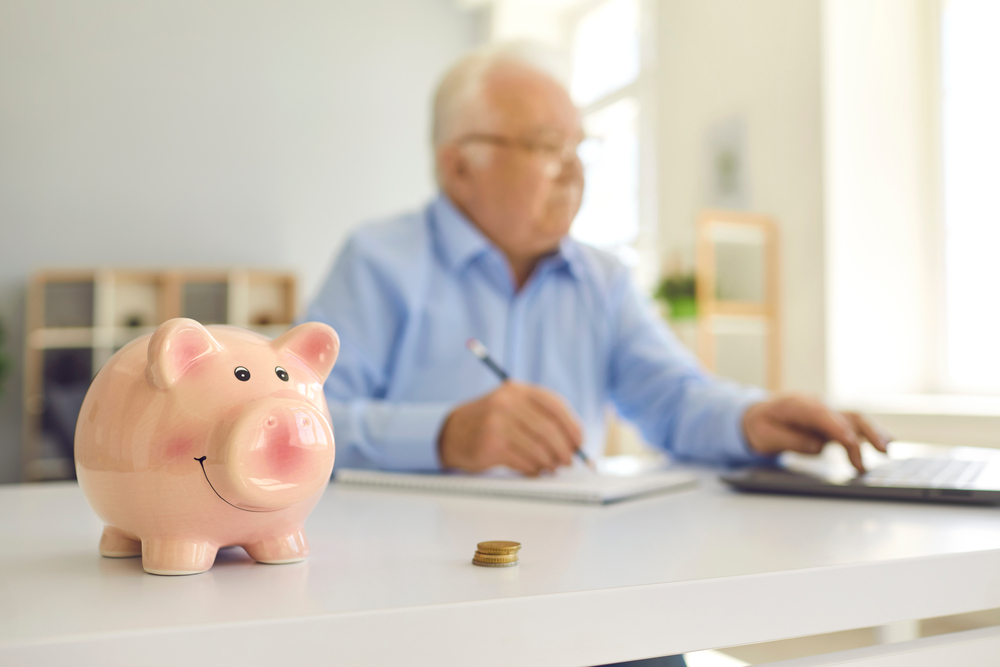 Piggy bank in soft focus on desk and retired man